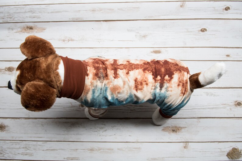May include: A brown and white dog wearing a blue and brown tie-dye pajama onesie with a brown collar.