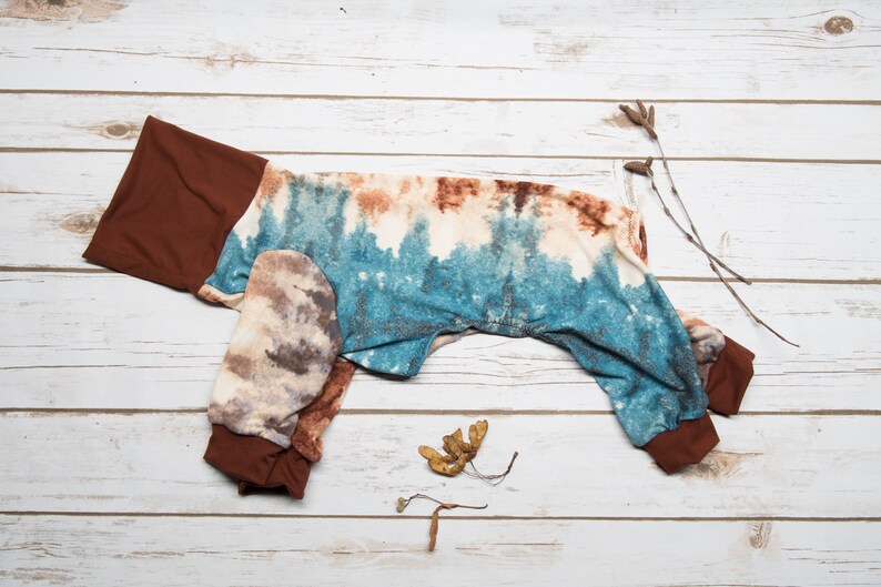 May include: A brown and blue tie-dye dog jumpsuit with brown cuffs. The jumpsuit is laid out flat on a white wooden surface.
