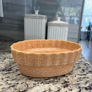 May include: An orange ceramic dish with a textured surface and a scalloped rim. Two white canisters with crystal-topped lids are in the background. The dish is on a granite countertop.