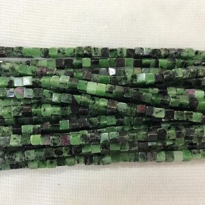 May include: A strand of green and black square-shaped gemstone beads. The beads are approximately 6mm in size and have a mottled appearance.