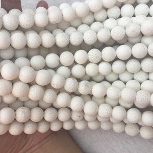 May include: Close-up of multiple strands of white, round beads. The beads have a textured, porous surface, and are strung together. The beads are a neutral white colour, and are likely used for jewellery making or crafting.