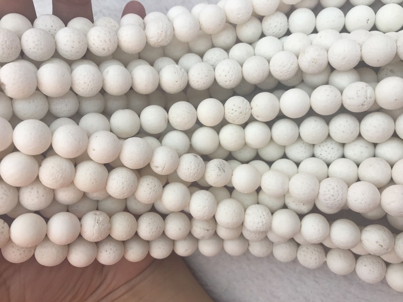 May include: Close-up of multiple strands of white, round beads. The beads have a textured, porous surface, and are strung together. The beads are a neutral white colour, and are likely used for jewellery making or crafting.