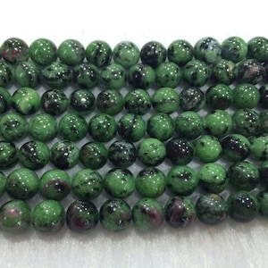 Puede incluir: Una hebra de cuentas de piedras preciosas verdes y negras. Las cuentas son redondas y tienen un acabado liso y pulido.