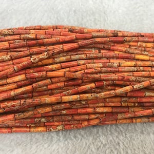 Puede incluir: Una hebra de cuentas de jaspe naranja y marrón, cada cuenta tiene forma de tubo rectangular.