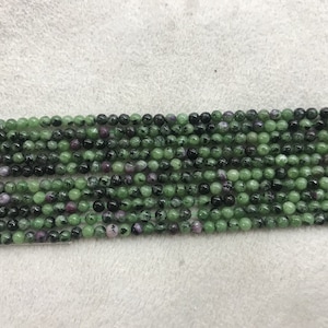 Op de afbeelding: Een streng groene en zwarte edelsteen kralen. De kralen zijn rond en hebben een gevlekt uiterlijk.