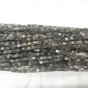 May include: A strand of gray and white square gemstone beads. The beads are faceted and have a translucent appearance.