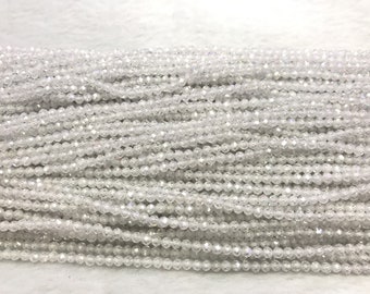 May include: A strand of white faceted glass beads. The beads are round and have a textured surface. The beads are strung on a clear thread.