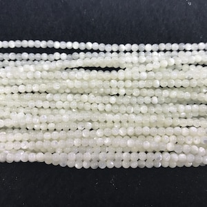 Könnte beinhalten: Eine Strähne weißer runder Perlen aus Mondstein. Die Perlen sind glatt und haben einen dezenten irisierenden Schimmer.