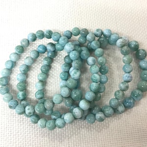 May include: Four bracelets made of round, light blue and green beads. The beads have a marbled appearance, with variations in color. The bracelets are arranged in a loose, overlapping pattern, showcasing the jewelry.
