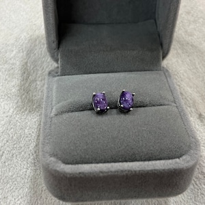 Puede incluir: Un par de pendientes de plata con piedras ovaladas de color púrpura.