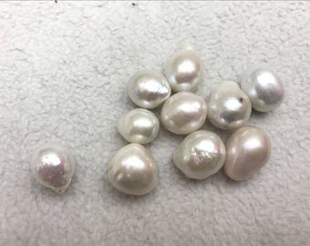 Pode incluir: Um grupo de dez pérolas brancas peroladas de forma irregular. As pérolas estão dispostas em um cacho sobre uma superfície branca texturizada.