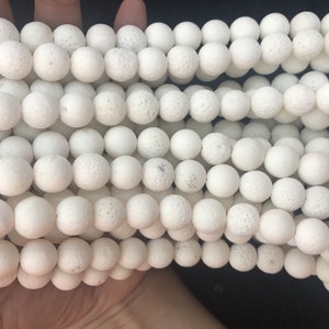 May include: Close-up of multiple strands of white, spherical beads. The beads have a textured, porous surface. They are consistent in size and likely made from a natural material. Suitable for jewellery making or craft projects.