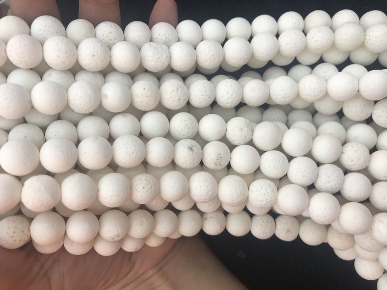 May include: Close-up of multiple strands of white, spherical beads. The beads have a textured, porous surface. They are consistent in size and likely made from a natural material. Suitable for jewellery making or craft projects.