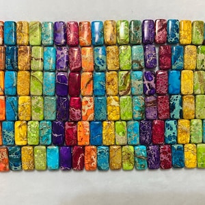 May include: A collection of rectangular beads arranged in a grid, featuring a variety of vibrant colours including purple, orange, blue, yellow, and green. Each bead displays a unique marbled pattern with intricate veining throughout the surface.