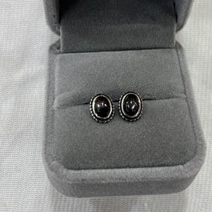 Könnte beinhalten: Ein Paar ovale Ohrringe mit schwarzen Edelsteinen, die in Silber gefasst sind.