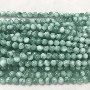 May include: A strand of light green round beads with a white marbled pattern. The beads are smooth and glossy.