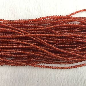 May include: A strand of small, round, orange carnelian beads. The beads are strung on a thin wire and are all approximately the same size.