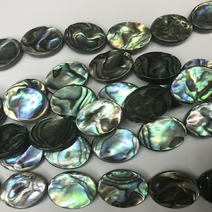 May include: Oval-shaped abalone shell beads in shades of green, blue, and black. The beads have a pearlescent sheen and are strung together to form a necklace or bracelet.