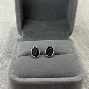Könnte beinhalten: Ein Paar silberne Ohrstecker mit ovalen schwarzen Edelsteinen.