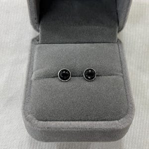 Könnte beinhalten: Ein Paar schwarze Onyx-Ohrstecker mit silbernen Fassungen in einer grauen Samt-Schmuckschatulle.