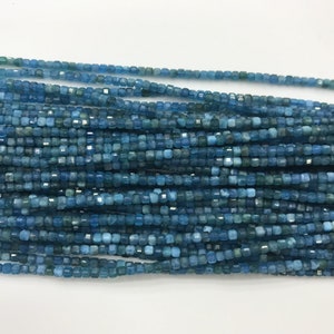 Puede incluir: Una hebra de cuentas de apatita azul, cada cuenta es de forma cuadrada y facetada. Las cuentas están enhebradas en un hilo transparente.