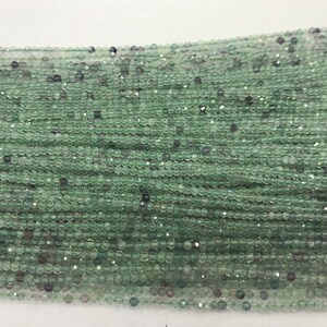 May include: A strand of light green faceted glass beads. The beads are round and have a slight shimmer to them.