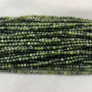 May include: A strand of green serpentine beads, each bead is round and has a speckled pattern.