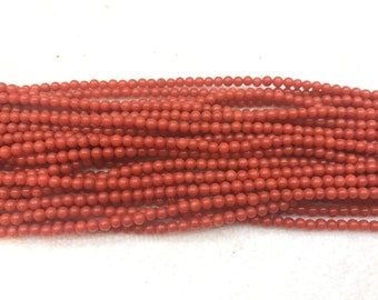 May include: A strand of bright red coral beads. The beads are round and smooth, and they are strung on a clear thread.