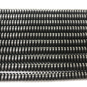 以下が含まれることがあります： 黒ヘマタイトビーズのストランド。各ビーズはファセットカットされており、わずかに丸みを帯びた形をしています。