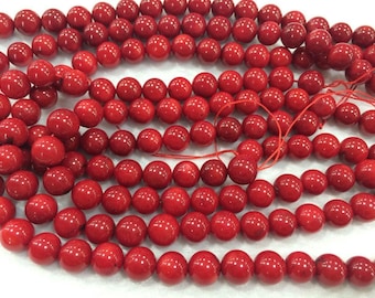 May include: A strand of bright red coral beads. The beads are round and smooth, and they are strung on a thin red thread.