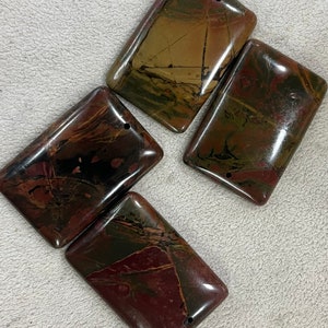 May include: Four rectangular gemstone pendants with a polished finish. The stones display dark red, brown, and green hues with natural veining. Each pendant has a small hole drilled at the top for stringing, ideal for jewellery.