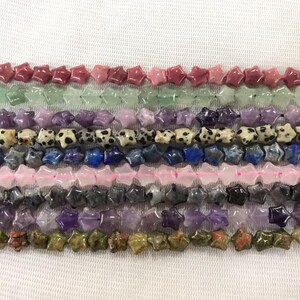Puede incluir: Una hebra de cuentas de piedras preciosas en forma de estrella en varios colores, incluyendo rosa, verde, morado, azul y marrón. Las cuentas están dispuestas en filas, creando una exhibición colorida y llamativa.