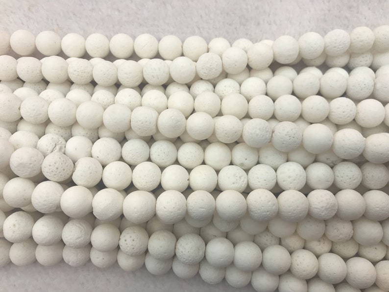 May include: Close-up of strands of white, round beads with a textured, porous surface. The beads are uniform in size and shape, creating a consistent pattern. The beads are likely used for jewellery making or crafting.