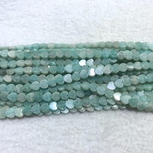 May include: Strands of heart-shaped beads in shades of pale blue and white. The beads have a slightly iridescent quality, and are strung together. The beads are likely made of a gemstone or other natural material.