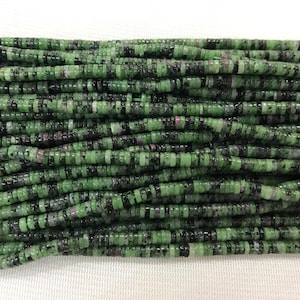May include: A strand of green, black, and pink gemstone beads. The beads are small and round, and they are strung together on a clear thread.