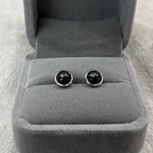 May include: A pair of black gemstone stud earrings in a grey velvet jewellery box.