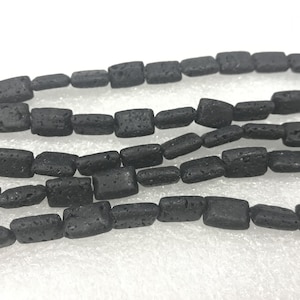 Puede incluir: Una hebra de cuentas de roca volcánica negra, cada cuenta tiene forma rectangular. Las cuentas están enhebradas para crear un collar o una pulsera.