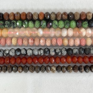 May include: A close-up of several strands of faceted gemstone beads in various colors. The beads include shades of brown, green, pink, gray, and red. The beads are strung together, showcasing their individual shapes and colors.