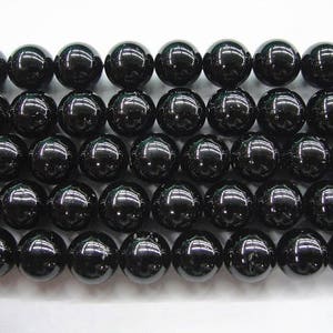 May include: A strand of black gemstone beads. The beads are round and smooth, and they are strung on a clear thread.
