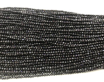 May include: A strand of black faceted gemstone beads. The beads are small and round, and they have a shiny, iridescent finish.