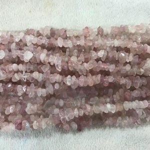 以下が含まれることがあります： ピンクのローズクォーツチップビーズのストランド。ビーズは不規則な形をしていて、自然なタンブル仕上げになっています。