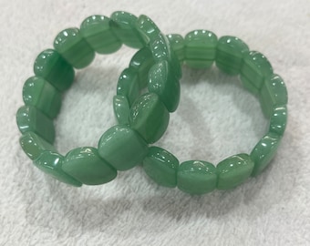 May include: Two green jade stone bracelets with a rounded, slightly oval shape. The bracelets are made of individual beads that are connected together.
