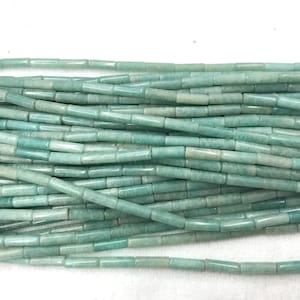 May include: A close-up of a pile of light teal-colored, cylindrical beads. The beads are strung together, creating a textured surface. The beads are uniform in size and shape, with a slightly glossy finish.