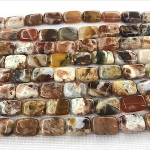 Puede incluir: Una hebra de cuentas de piedra de ágata de color marrón, naranja y blanco. Las cuentas son rectangulares y tienen un acabado pulido.