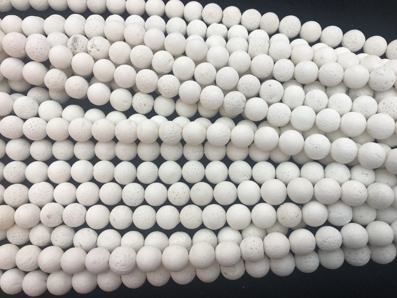 May include: A close-up shot of numerous white, spherical beads with a textured surface. The beads are tightly packed together, filling the image. They appear to be made from a porous material, and are likely used for jewellery making.