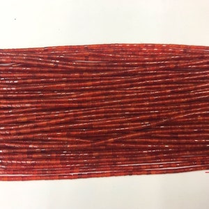 May include: A close-up view of numerous strands of small, rectangular, reddish-brown beads. The beads are tightly packed together, creating a textured surface. The beads appear to be made of glass or a similar material, with a slight sheen. The overall effect is of a rich, earthy tone.