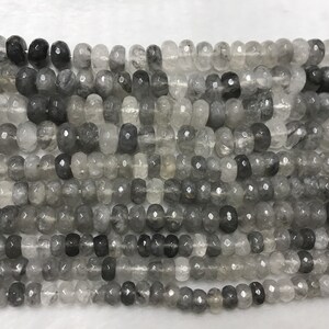 Könnte beinhalten: Eine Strähne aus grauen und klaren facettierten Edelsteinperlen. Die Perlen sind rund und haben eine leicht unregelmäßige Form.