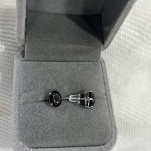Könnte beinhalten: Ein Paar schwarze Edelstein-Ohrstecker in einer grauen Samt-Schmuckschatulle.