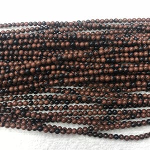 May include: A strand of brown and black speckled round beads. The beads are approximately 6mm in diameter and are strung on a clear elastic cord.