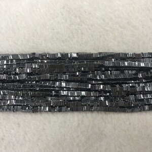 Puede incluir: Una hebra de cuentas de hematites negras, cada cuenta es una pequeña forma rectangular plana.